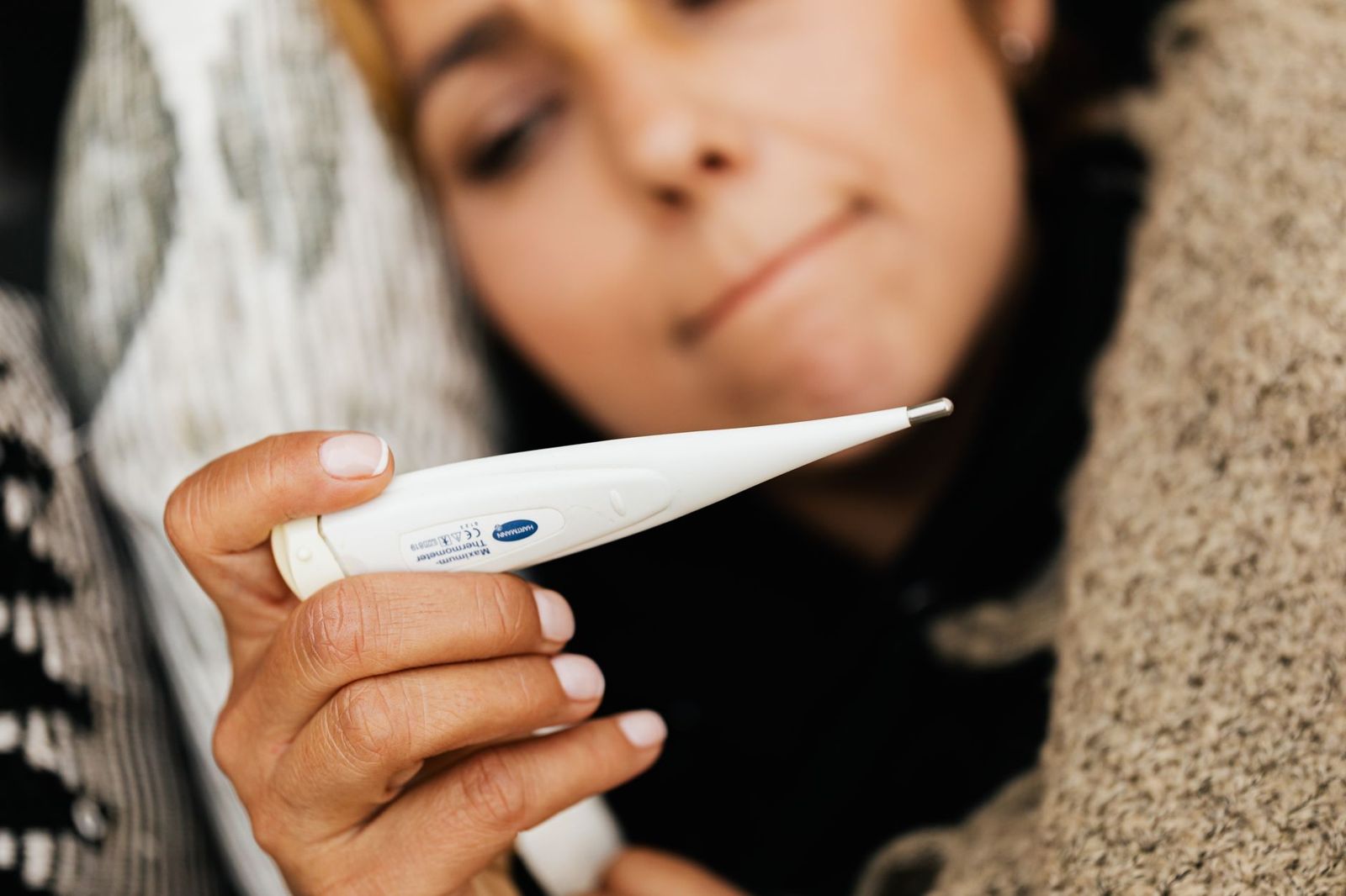 A woman wrapped in a blanket checking her temperature