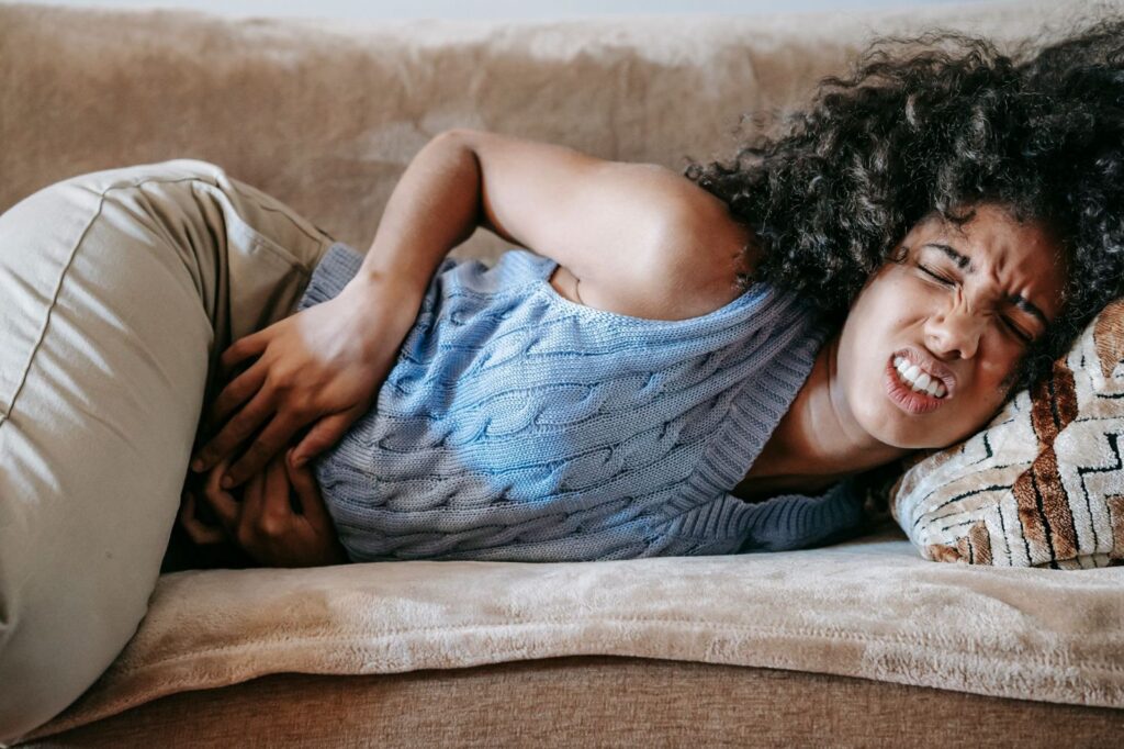 A woman lying on a sofa holding her stomach in pain
