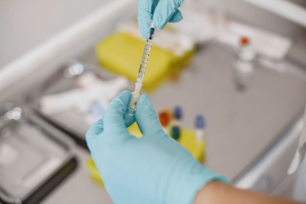 A gloved hand holding a syringe beside a medical tray