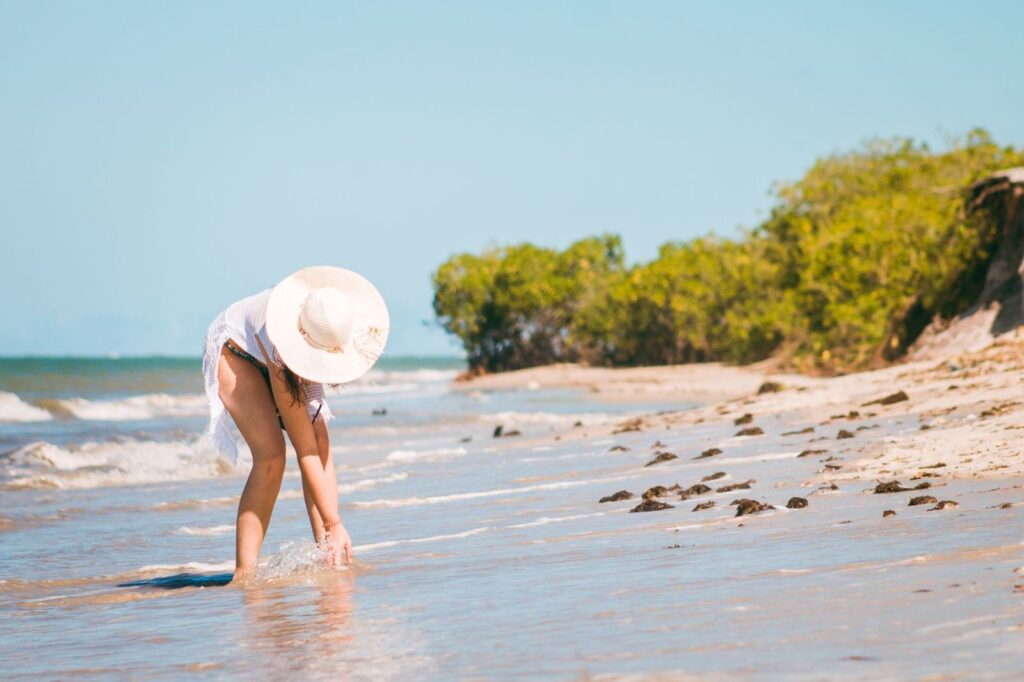 A woman in a sun hat at the water's edge on a bright beach