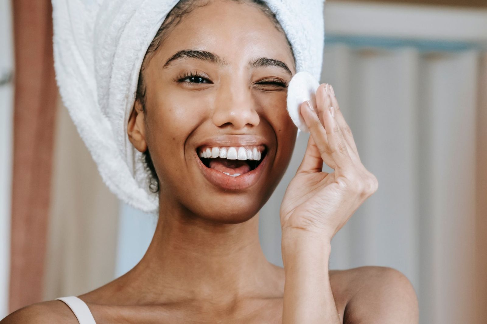 A smiling woman cleansing her face with a cotton pad