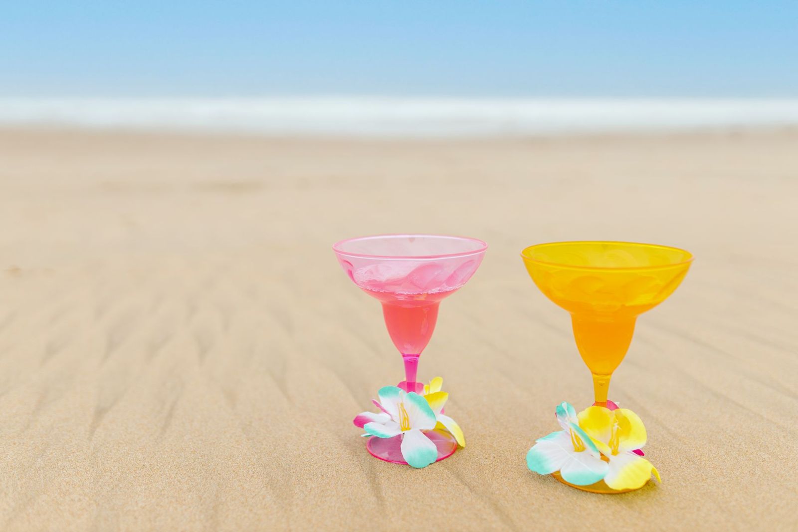 Two cocktails standing in the sand on a beach
