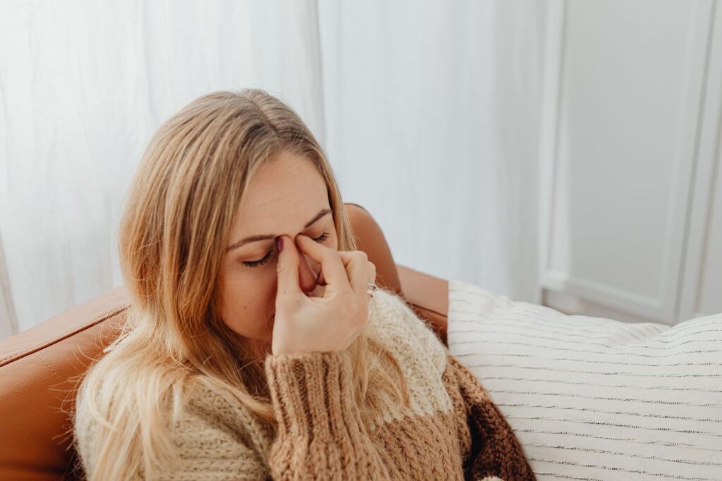 A woman holding the bridge of her nose, feeling unwell