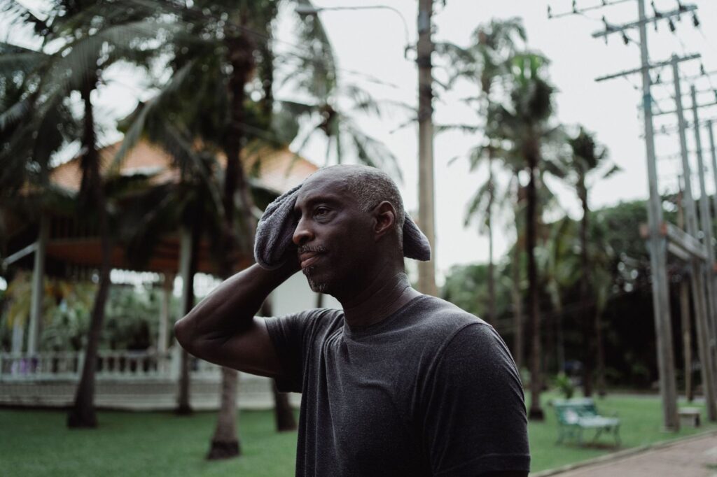 A man wiping his head in the heat under palm trees