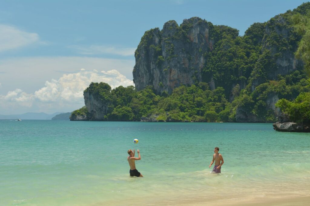Two men playing beach volleyball on Ao Nang beach below limestone cliffs