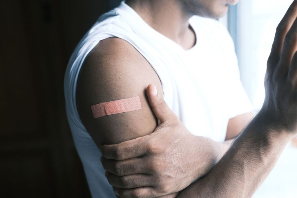 A man holding his arm where a plaster covers a small puncture