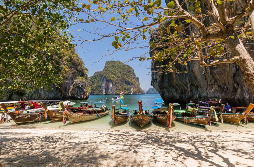 Longtail boats lined up on a beach between limestone cliffs
