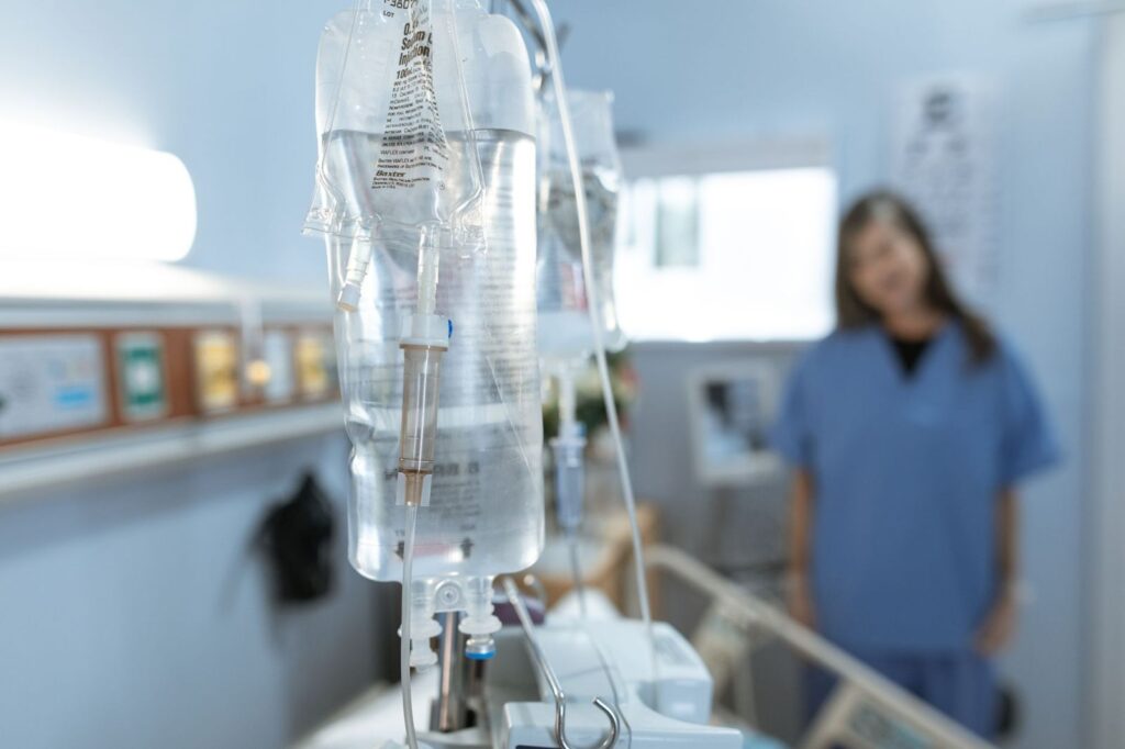 An IV bag on a stand with a nurse in the background