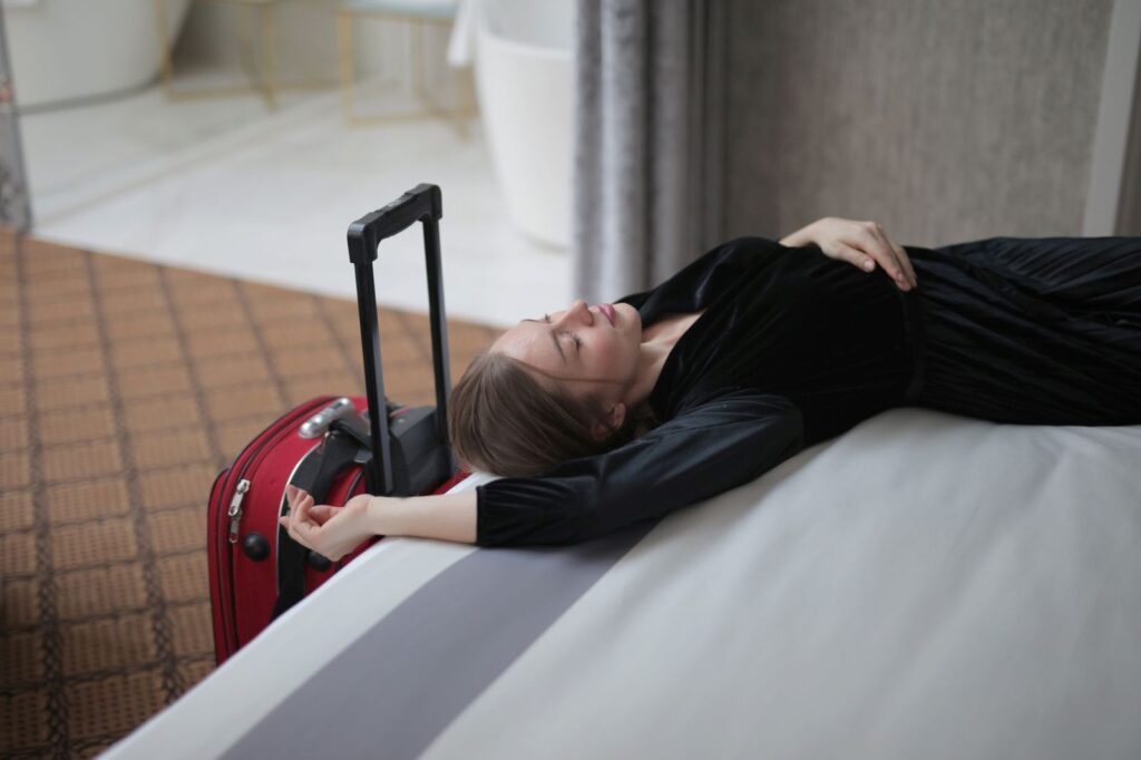 A tired traveller lying on a hotel bed beside her suitcase