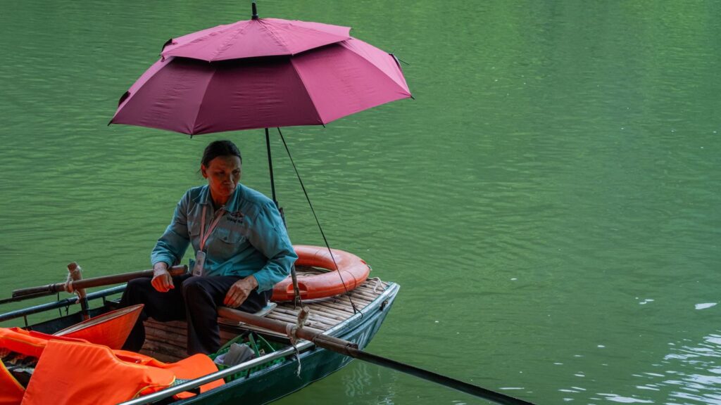 A man rowing a small boat under a sun umbrella
