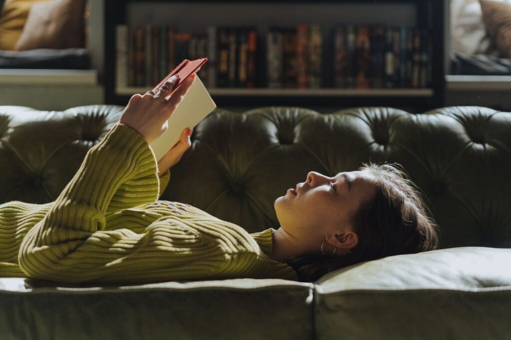 A woman reading a book while resting on a sofa