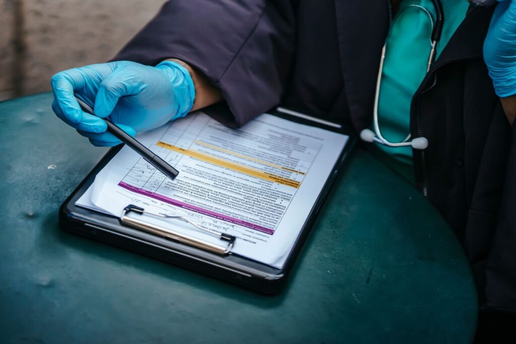 A gloved hand filling in a medical form on a clipboard