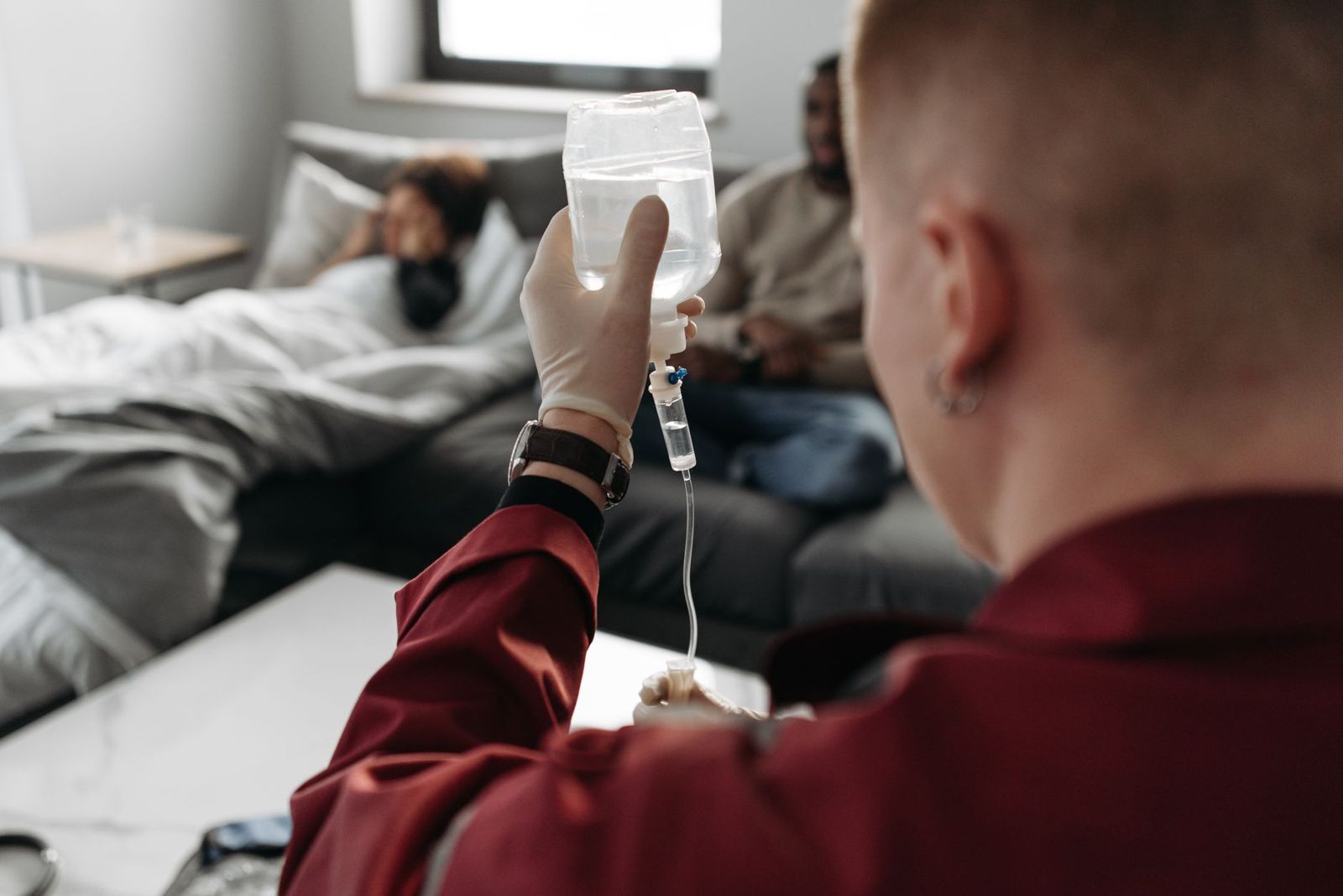 Someone holding an IV bag while a patient rests on a sofa