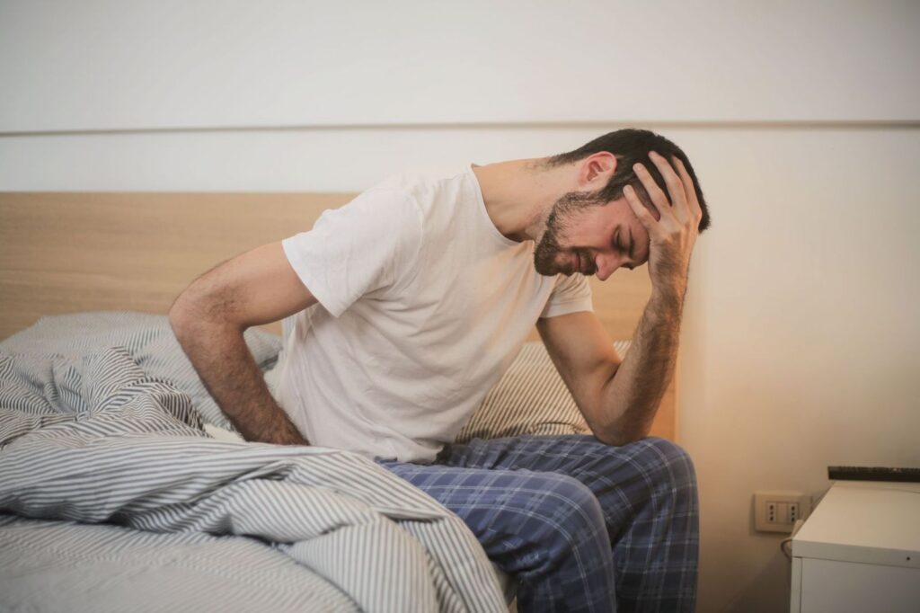 A man sitting on the edge of his bed with his head in his hands
